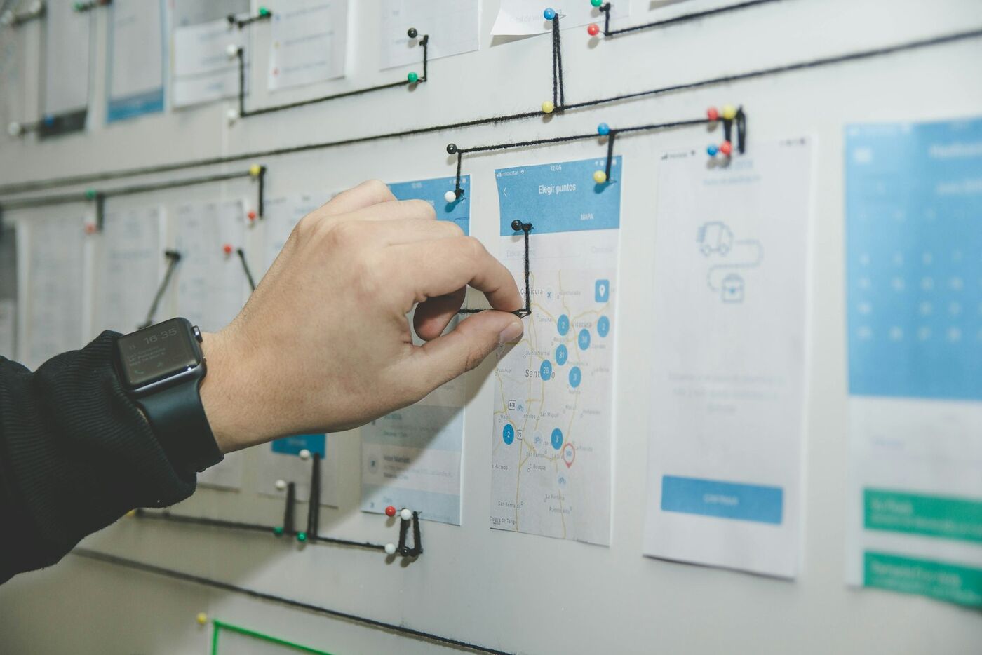 Hand connecting the steps of a process map pinned to a wall with string