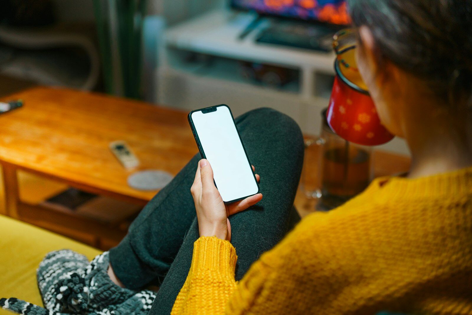 Woman relaxing at home with a cup of tea, reading a message on her phone