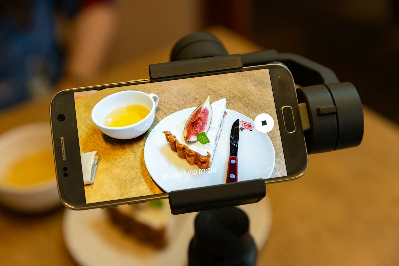 A smartphone on a stabiliser filming a slice of fig tart and a cup of tea for a short-form video ad