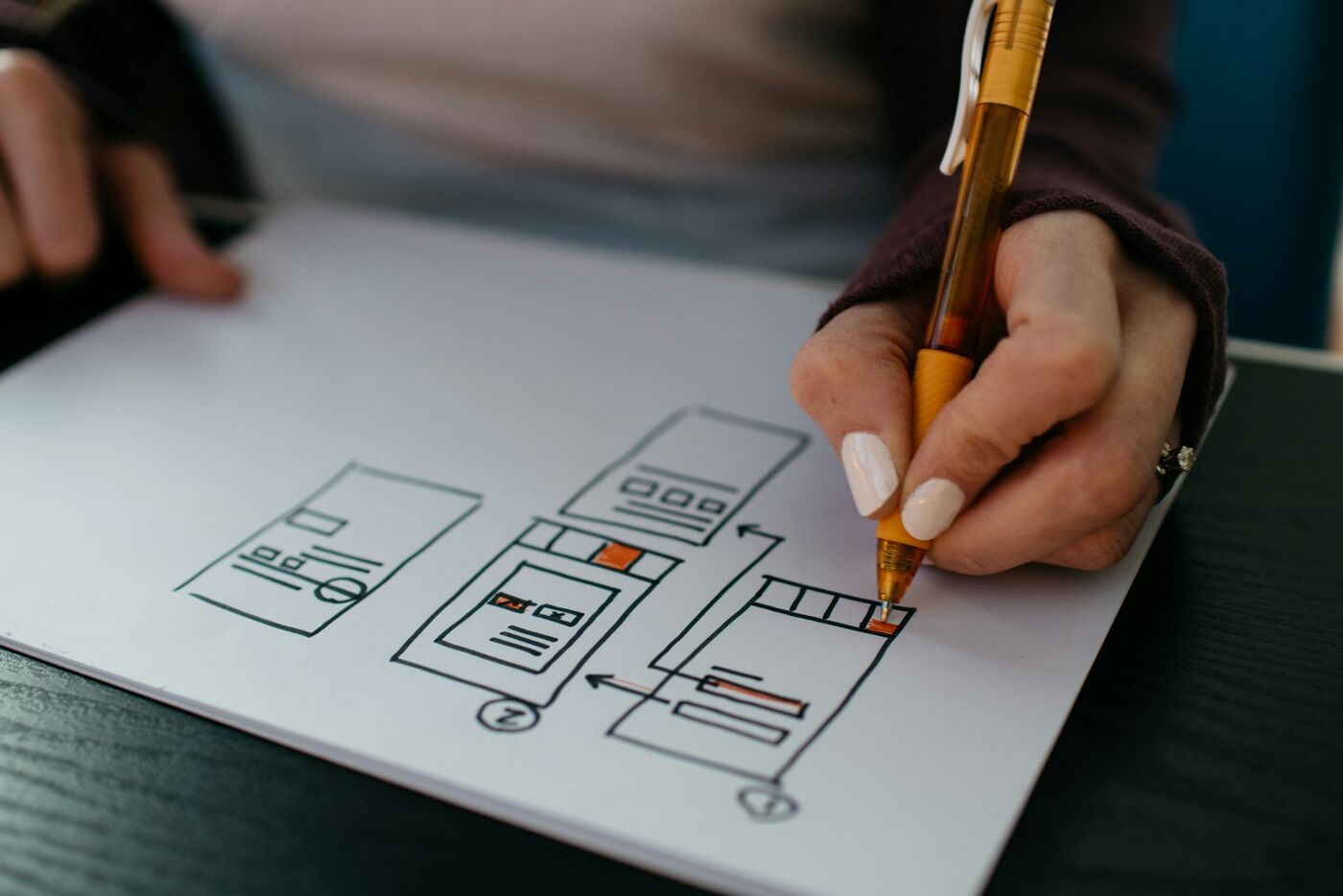 Designer sketching a mobile website wireframe and user flow by hand on paper