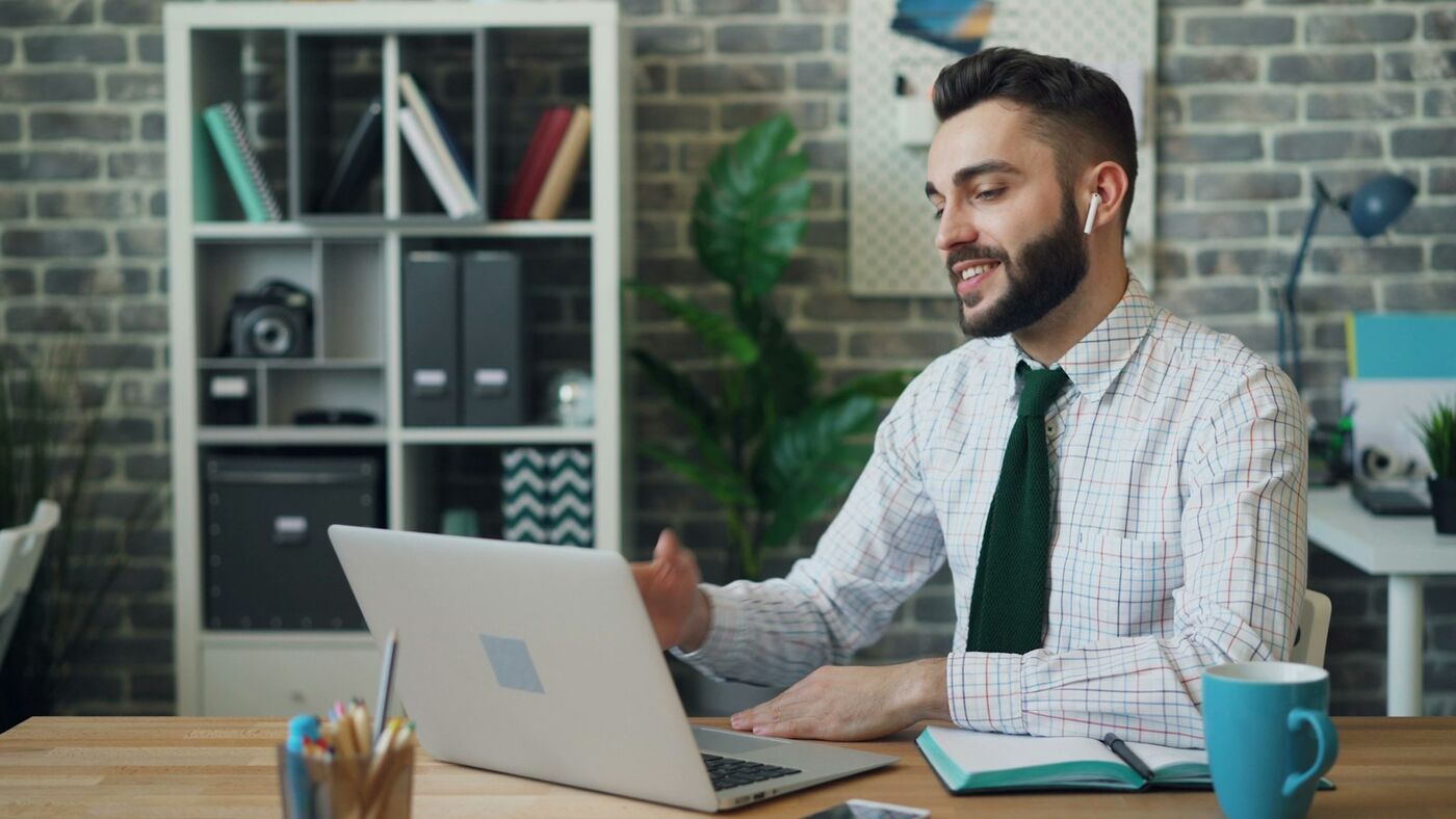 Smiling man on a video call at his laptop in a bright office